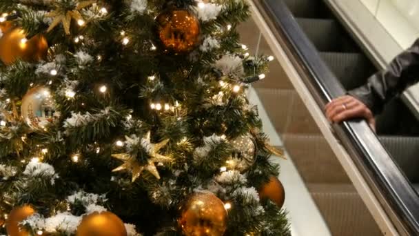 Gyönyörűen díszített karácsonyfa nagy arany és ezüst golyó, a csillagok, a koszorúkat és a mesterséges hó állandó, a bevásárlóközpont, vagy a bevásárlóközpont, emberek a mozgólépcsõn van elhaladó — Stock videók