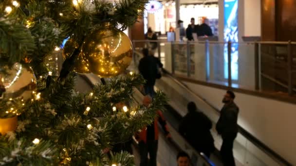 Nürnberg, Deutschland - 1. Dezember 2018: Schön geschmückter Weihnachtsbaum auf dem Hintergrund zweier Rolltreppen in einem Einkaufszentrum, auf denen die Käufer stehen — Stockvideo