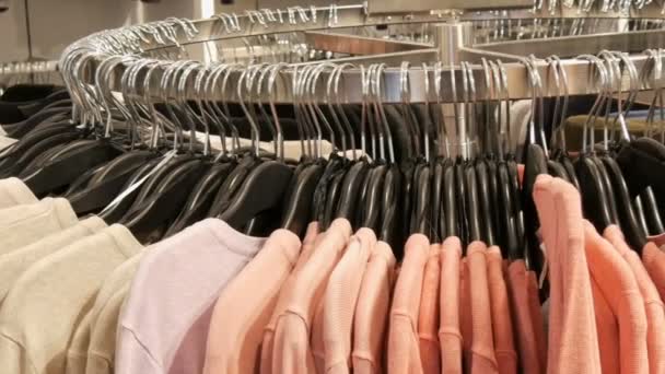 Κομψά ρούχα που κρέμονται στη γραμμή στις κρεμάστρες σε ένα κατάστημα ιματισμού σε ένα εμπορικό κέντρο. — Αρχείο Βίντεο
