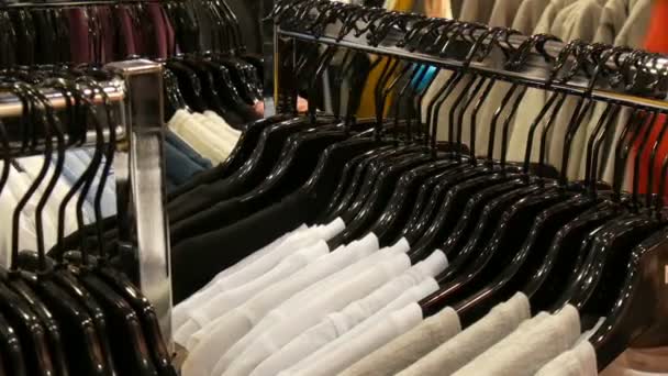 Stylowe ubrania wiszące w wierszu na wieszakach w Sklep odzieżowy w centrum handlowym. — Wideo stockowe