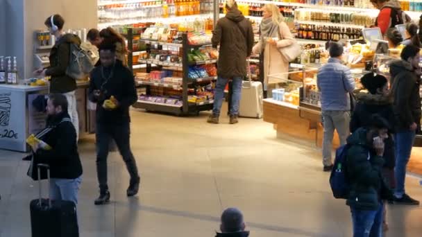 Múnich, Alemania - 2 de diciembre de 2018: Apresurando a los pasajeros con maletas a caminar cerca de una pequeña tienda de comestibles en la estación principal de tren de Múnich . — Vídeo de stock