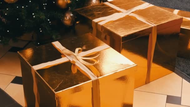 Grandes cajas de regalo, regalo de color oro bajo el árbol de Navidad en el centro comercial. Navidad y Año Nuevo decoración de regalos. Caja de regalo de oro con cinta de satén de oro . — Vídeos de Stock