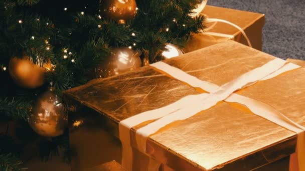 Grandes cajas de regalo, regalo de color oro bajo el árbol de Navidad en el centro comercial. Navidad y Año Nuevo decoración de regalos. Caja de regalo de oro con cinta de satén de oro . — Vídeos de Stock