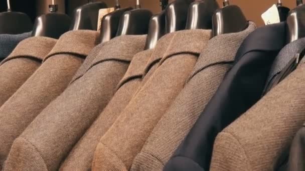 Стильные куртки из коричневой шерсти висят на вешалках в торговом центре . — стоковое видео