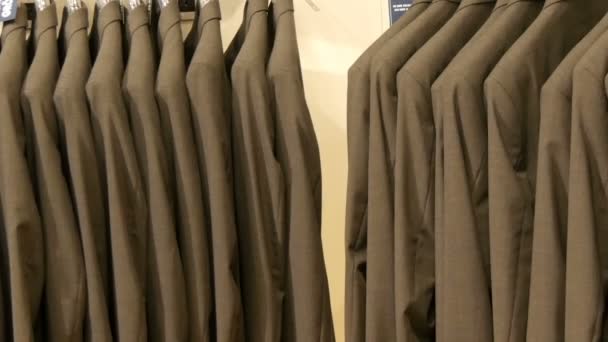 Number of identical-colored mens suits hanging on a hanger in a clothing store in a mall — Stock Video