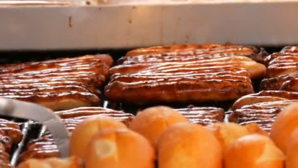 Christmas market, national German sausages are grilled, next to buns. Womens hands turn Nuremberg sausages with help of special tweezers — Stock Video