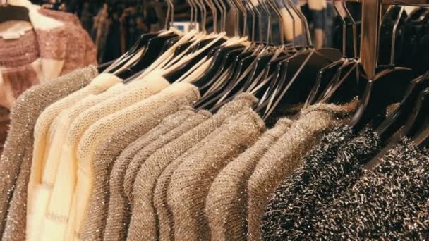 Rząd swetry puszyste piękne damskie ciepłe szarości, czerni i bieli są wiszące na wieszakach czarna w sklepie oraz centrum handlowego mall. Modna kolekcja ciepłe ubrania. — Wideo stockowe