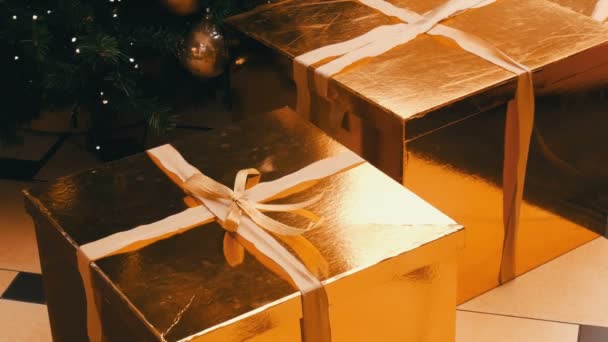 Large gift boxes, present of gold color under the Christmas tree in the mall. Christmas and New Years gift decor. Gift gold box with gold satin ribbon. — Stock Video