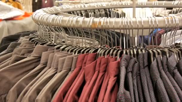 Fila de várias camisas masculinas na moda em um enorme cabide na loja de roupas masculinas no centro comercial . — Vídeo de Stock