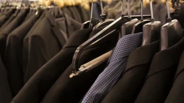 Ряд различных модных мужчин черные куртки и рубашки на вешалке в мужском магазине одежды в торговом центре . — стоковое видео