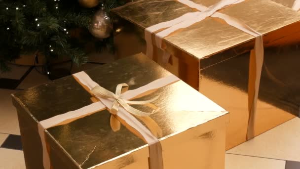 Large gift boxes, present of gold color under the Christmas tree in the mall. Christmas and New Years gift decor. Gift gold box with gold satin ribbon. — Stock Video