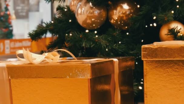 Grote geschenkverpakkingen, presenteren van gouden kleur onder de kerstboom in het winkelcentrum. Kerstmis en Nieuwjaar cadeau decor. De doos van de gift goud met gouden satijn lint. — Stockvideo