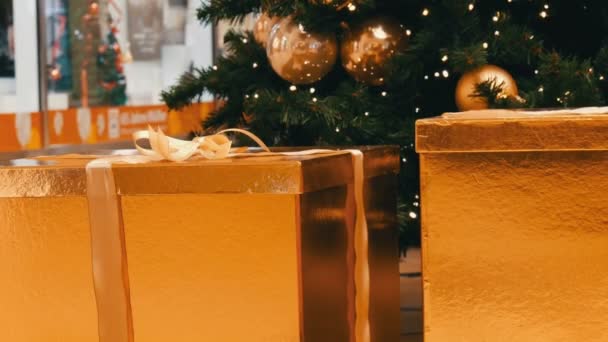 Grandes caixas de presente, presente de cor dourada sob a árvore de Natal no shopping. Decoração de presente de Natal e Ano Novo. Caixa de presente de ouro com fita de cetim ouro . — Vídeo de Stock