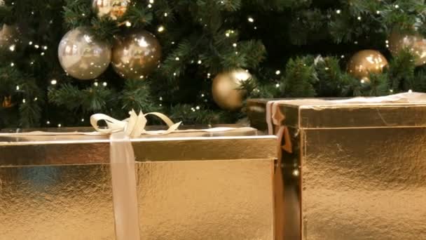 Grandes cajas de regalo, regalo de color oro bajo el árbol de Navidad en el centro comercial. Navidad y Año Nuevo decoración de regalos. Caja de regalo de oro con cinta de satén de oro . — Vídeos de Stock