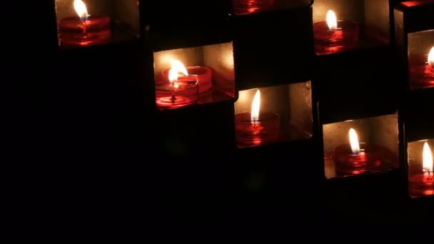 Belas velas vermelhas da igreja para orações em nichos especiais em um templo católico no fundo preto — Vídeo de Stock