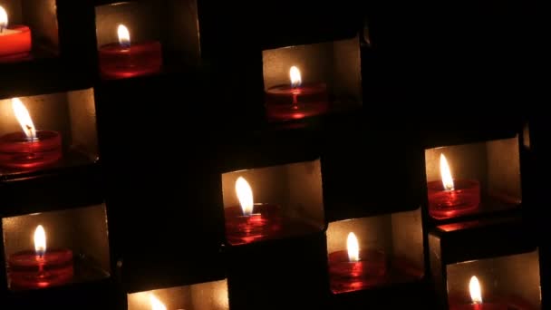 Красиві червоні церковні свічки для молитви в спеціальних нішах в католицькому храмі на чорному тлі — стокове відео