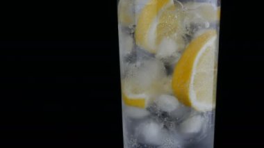 Siyah bir arka planda buz küpleri ve soğuk soda ile uzun bir cam dilimlenmiş limon görünümü yakın. Ferahlatıcı limonata kabarcıklar.