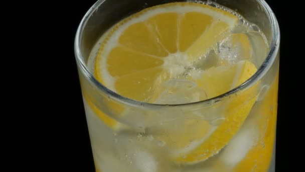 Limón en rodajas en un vaso largo con cubitos de hielo y refrescos fríos sobre un fondo negro vista de cerca. Refrescante Limonada Burbujas . — Vídeos de Stock