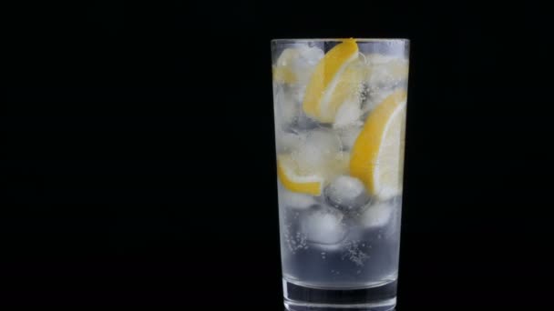 Gesneden citroen in een lang glas met ijsblokjes en koude soda op een zwarte achtergrond. Verfrissende limonade bubbels. — Stockvideo