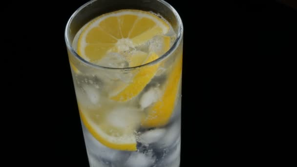Limón en rodajas en un vaso largo con cubitos de hielo y refrescos fríos sobre un fondo negro vista de cerca. Refrescante Limonada Burbujas . — Vídeos de Stock