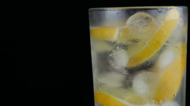 Limón en rodajas en un vaso largo con cubitos de hielo y refrescos fríos sobre un fondo negro vista de cerca. Refrescante Limonada Burbujas . — Vídeo de stock