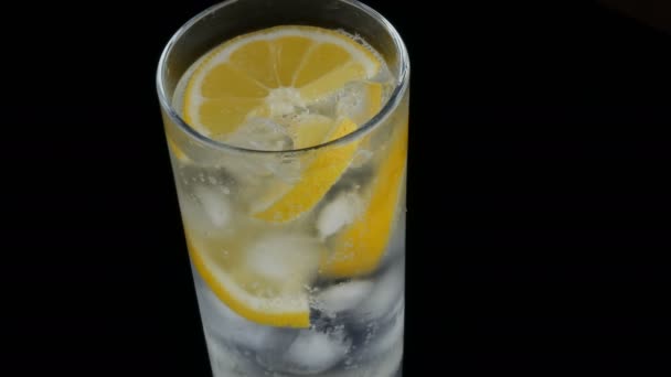 Limón en rodajas en un vaso largo con cubitos de hielo y refrescos fríos sobre un fondo negro vista de cerca. Refrescante Limonada Burbujas . — Vídeo de stock