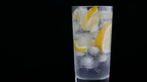 Trancher le citron dans un long verre avec des glaçons et du soda froid sur un fond noir. Bulles de limonade rafraîchissantes . — Video