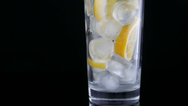 Vaso largo con rodajas de limón y cubitos de hielo sobre fondo negro . — Vídeos de Stock