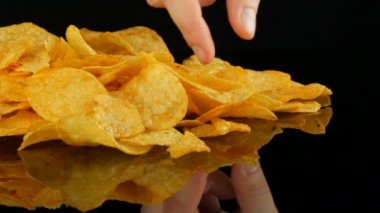Kadın eller patates cips rastgele siyah bir arka planda dağınık bir ayna yüzeyi üzerinde yalan almak. Zararlı yiyecekler, Fast Food.