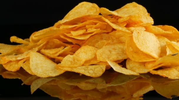 Potatis chips ligger på en spegel yta slumpmässigt utspridda på en svart bakgrund. Skadlig mat, snabbmat — Stockvideo