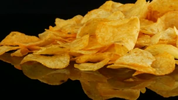 Potatis chips ligger på en spegel yta slumpmässigt utspridda på en svart bakgrund. Skadlig mat, snabbmat roterande — Stockvideo