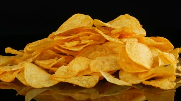 Potatis chips ligger på en spegel yta slumpmässigt utspridda på en svart bakgrund. Skadlig mat, snabbmat — Stockvideo