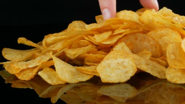 Patates cips rasgele siyah bir arka planda dağılmış bir ayna yüzeyi üzerinde yatıyor. Zararlı yiyecekler, Fast Food — Stok video