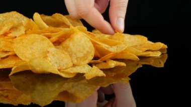Kadın eller patates cips rastgele siyah bir arka planda dağınık bir ayna yüzeyi üzerinde yalan almak. Zararlı yiyecekler, Fast Food.