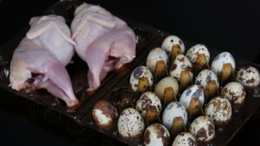 Siyah bir arka planda bıldırcın yumurtalarının yanında plastik kahverengi bir tepsi içinde bıldırcın taze et. Kadın elleri tepsiye yumurta alır.