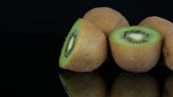 Vista elegante de la fruta madura en rodajas y kiwi entero en una superficie de espejo sobre fondo negro en el estudio — Vídeos de Stock