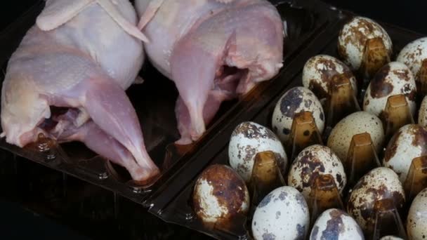 Fresh meat of quail in a plastic brown tray next to the quail eggs on a black background. — Stock Video