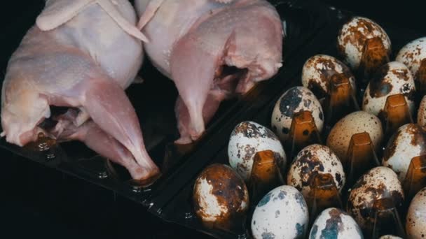 Carne fresca di quaglia in un vassoio di plastica marrone accanto alle uova di quaglia su uno sfondo nero . — Video Stock