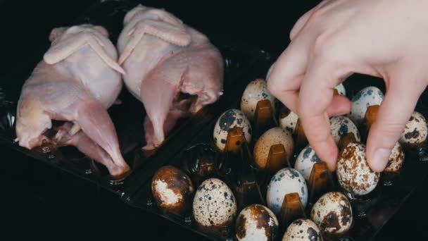 Carne fresca de codorna em uma bandeja marrom de plástico ao lado dos ovos de codorna em um fundo preto. As mãos femininas colocam os ovos na bandeja . — Vídeo de Stock