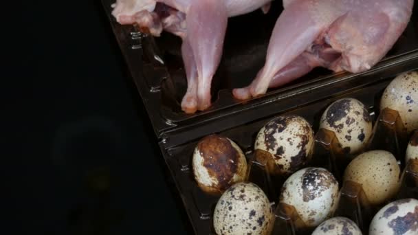 Carne fresca di quaglia in un vassoio di plastica marrone accanto alle uova di quaglia su uno sfondo nero . — Video Stock