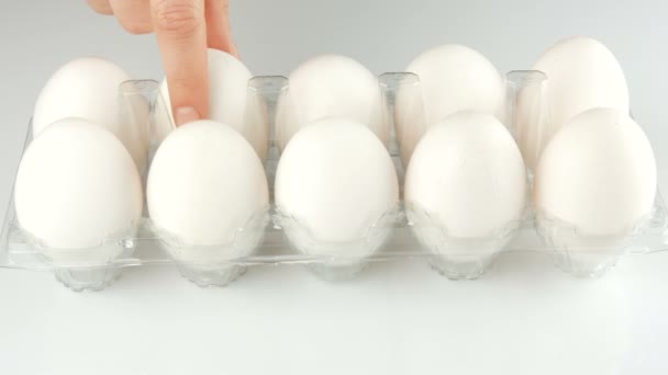Nagy fehér csirke tojás átlátszó műanyag tálcát fehér alapon. Női kéz érint minden a tojásokat a tálcába. — Stock videók