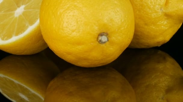 Stora färska gula citroner på svart spegel yta på en svart bakgrund närbild. — Stockvideo