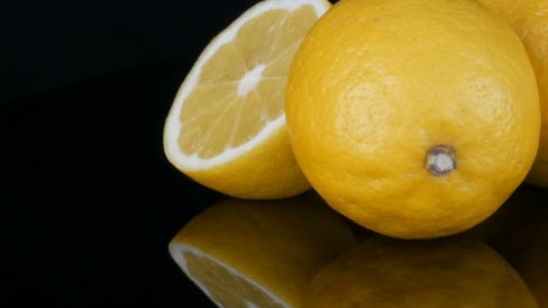 Big fresh yellow lemons on black mirror surface on a black background close up view. — Stock Video