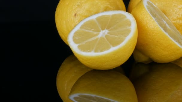 Большие свежие желтые лимоны на поверхности черного зеркала на черном фоне . — стоковое видео