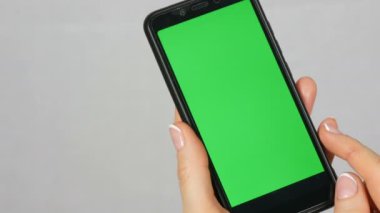 Güzel bir manikür ile bakımlı düzgün kadın eller stüdyoda beyaz arka plan üzerinde yeşil ekran veya krom anahtar ile siyah bir smartphone tutun