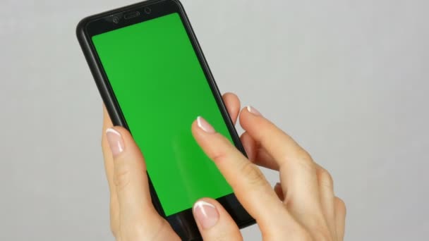 Bem preparado mãos femininas puras com uma bela manicure segurar um smartphone preto com uma tela verde ou chave de cromo no fundo branco no estúdio — Vídeo de Stock