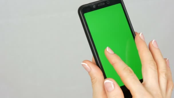 Bem preparado mãos femininas puras com uma bela manicure segurar um smartphone preto com uma tela verde ou chave de cromo no fundo branco no estúdio — Vídeo de Stock