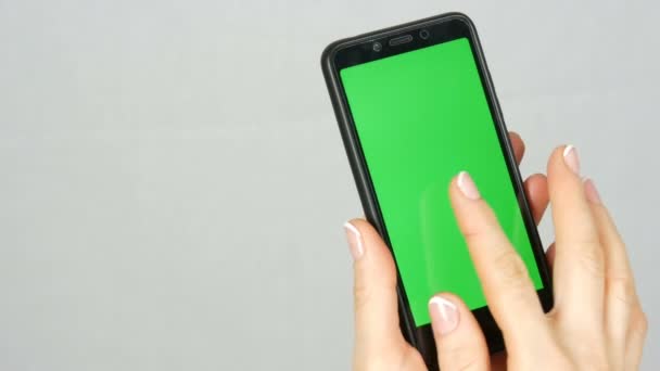 Las manos femeninas pulcras bien arregladas con una hermosa manicura sostienen un teléfono inteligente negro con una pantalla verde o una tecla de cromo sobre fondo blanco en el estudio — Vídeo de stock
