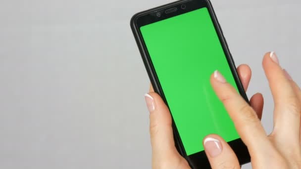 Las manos femeninas pulcras bien arregladas con una hermosa manicura sostienen un teléfono inteligente negro con una pantalla verde o una tecla de cromo sobre fondo blanco en el estudio — Vídeos de Stock