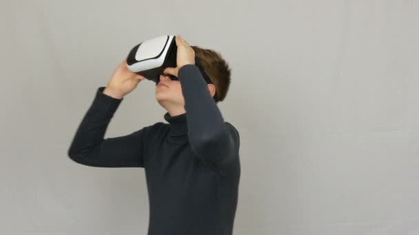 Menino adolescente olha para os óculos de realidade virtual branco ou VR e se diverte em um fundo branco no estúdio. O futuro é agora . — Vídeo de Stock